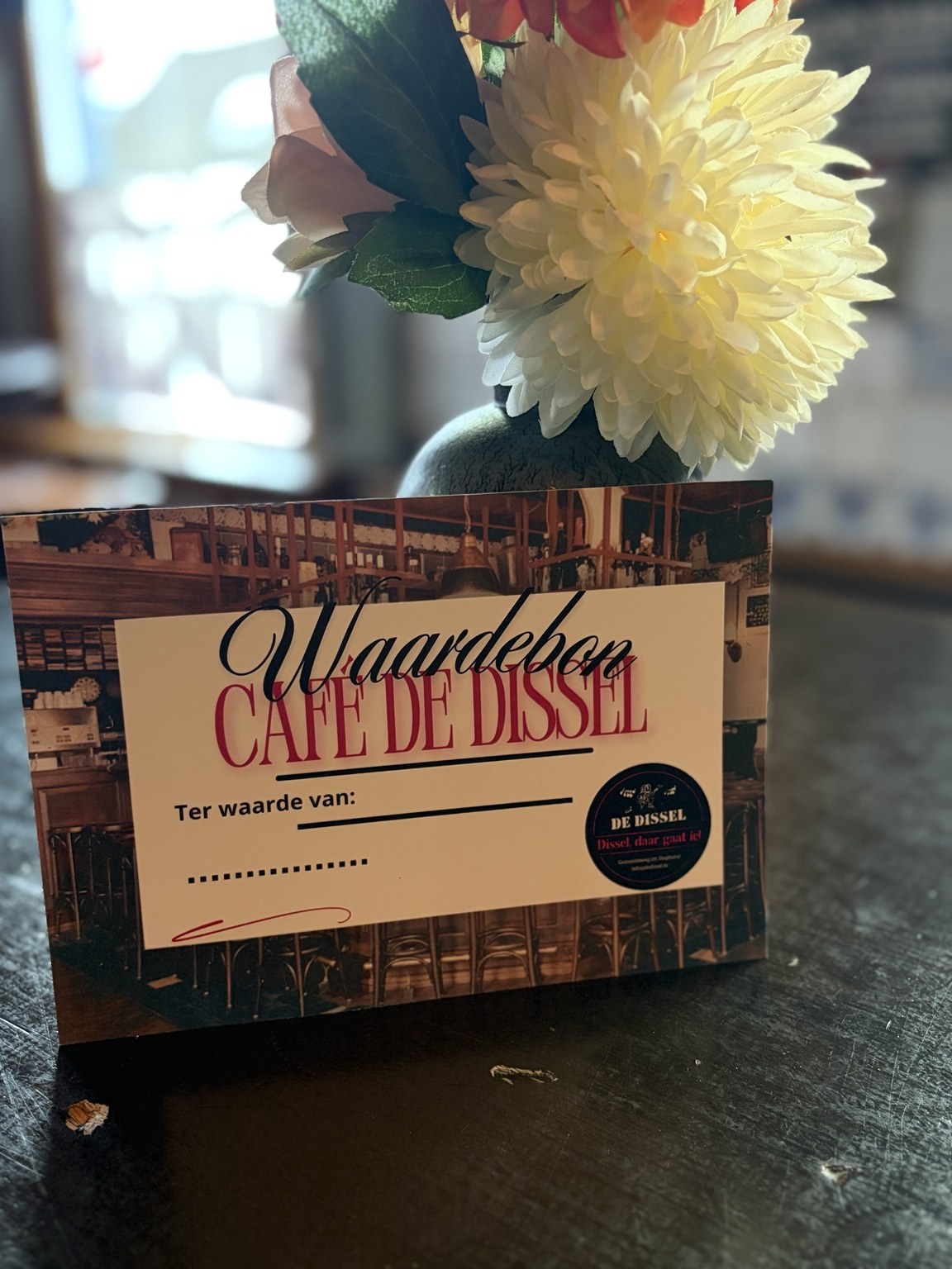 De waardebon van Café De Dissel op een tafel naast een vaas met bloemen